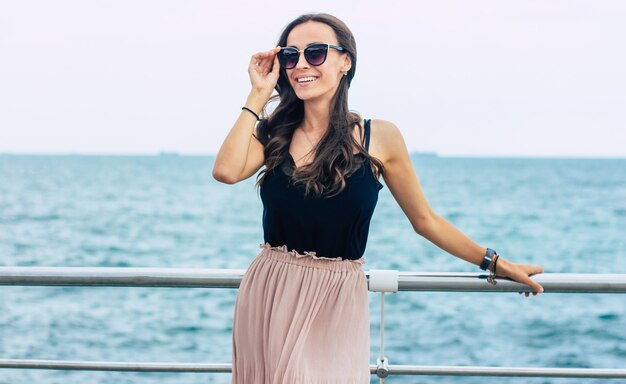 Hermosa mujer joven en gafas de sol y vestido en barco de crucero de lujo. Mujer de vacaciones de crucero disfrutando de viajes en el mar. Mujer feliz libre mirando al mar