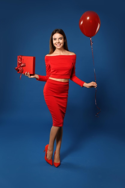 Hermosa mujer joven con globo y regalo para el Día de San Valentín sobre fondo de color