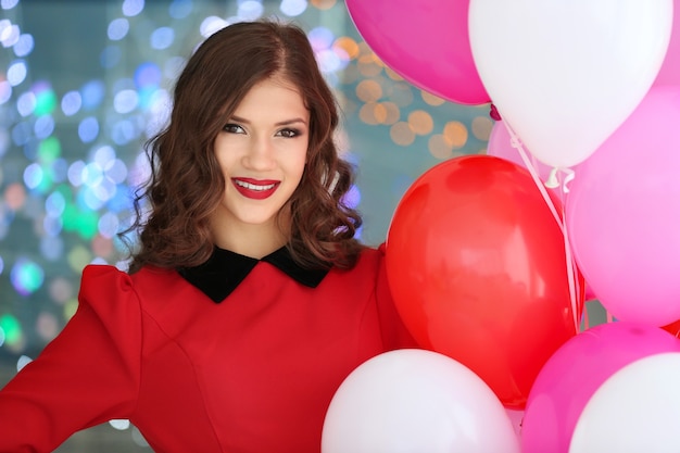 Hermosa mujer joven con globos de aire sobre fondo de luces borrosas