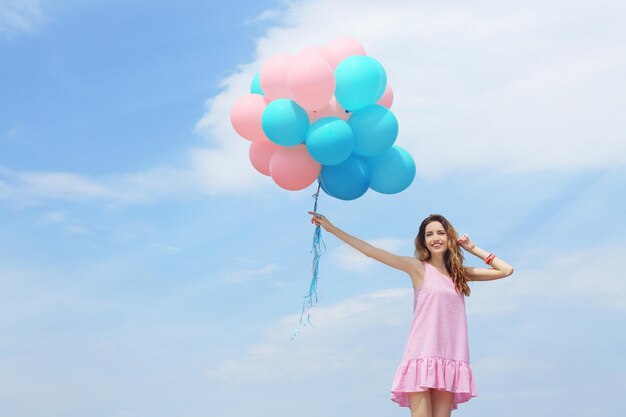 Hermosa mujer joven con globos de colores contra el cielo azul