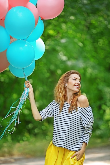 Hermosa mujer joven con globos de colores en el parque