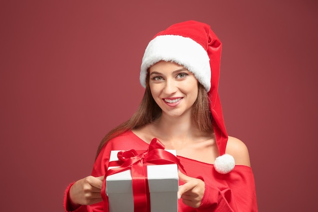 Hermosa mujer joven con gorro de Papá Noel con caja de regalo, sobre fondo de color