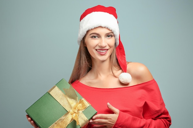 Hermosa mujer joven con gorro de Papá Noel con caja de regalo, sobre fondo de color