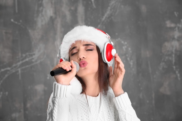 Hermosa mujer joven con gorro de Papá Noel cantando canciones de Navidad sobre fondo grunge