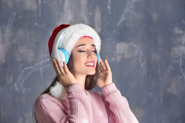 Hermosa mujer joven con gorro de Papá Noel escuchando música navideña sobre fondo grunge