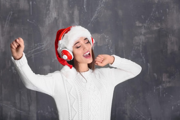 Hermosa mujer joven con gorro de Papá Noel escuchando música navideña sobre fondo grunge