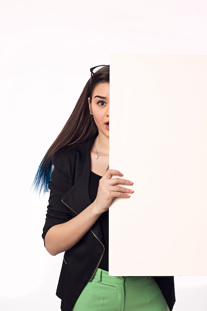 Foto hermosa mujer joven con gran cartel vacío en la pared blanca