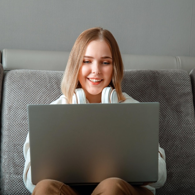 Hermosa mujer joven hace trabajo remoto estudio en línea desde casa a través de una computadora portátil Adolescente tiene un espacio de trabajo conveniente con computadora portátil Adolescente en una acogedora oficina en casa en un sofá independiente trabajo remoto Plaza