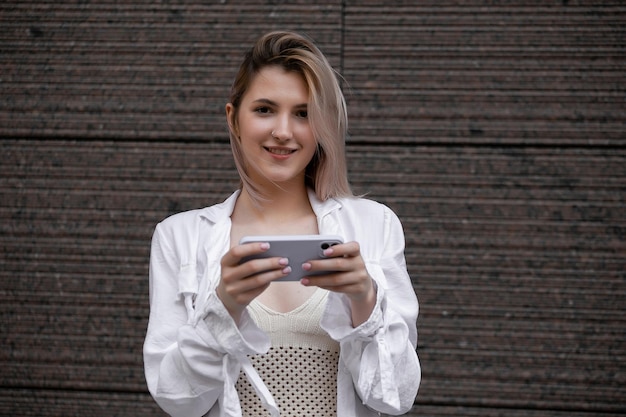 Foto hermosa mujer joven hermosa con mensajes de cabello rubio en el teléfono inteligente en el fondo de la calle de la ciudad chica guapa que tiene una conversación de teléfono inteligente en la calle de la ciudad