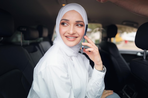 Hermosa mujer joven en hijab sentada en un coche y hablando por teléfono