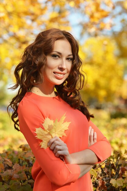 Hermosa mujer joven con hojas posando en el parque otoño