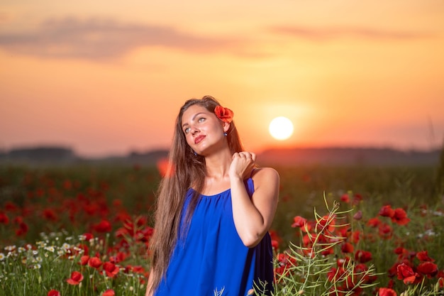 Hermosa mujer joven jugando con la bola del sol mientras está de pie en el campo de amapolas en la cálida luz del atardecer