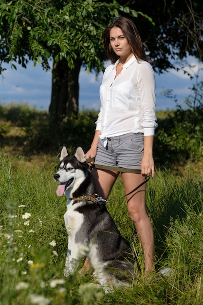 Hermosa mujer joven jugando con gracioso perro husky al aire libre en el parque