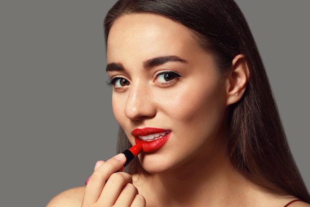 Hermosa mujer joven con lápiz labial brillante en espacio gris