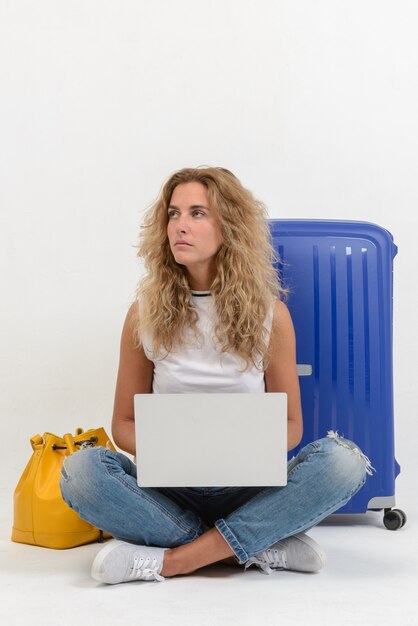 Hermosa mujer joven con laptop y maleta en pared blanca