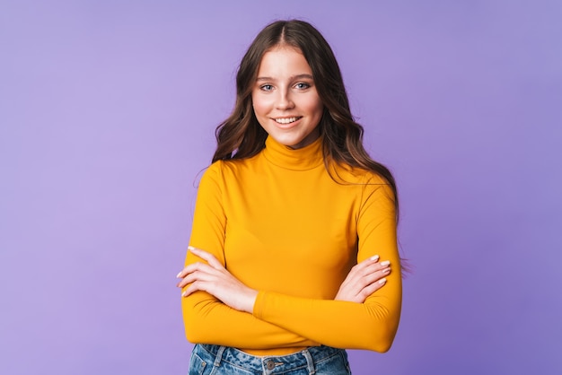 Hermosa mujer joven con largo cabello castaño sonriendo y posando en la pared púrpura