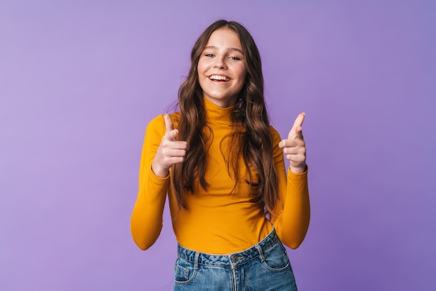 Hermosa mujer joven con largo cabello castaño sonriendo y señalando con el dedo a usted aislado