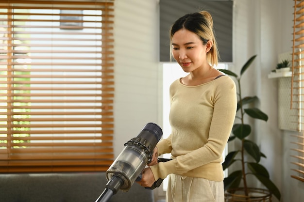 Hermosa mujer joven limpiando el piso con una aspiradora inalámbrica para eliminar los gérmenes y la suciedad Concepto de tareas domésticas