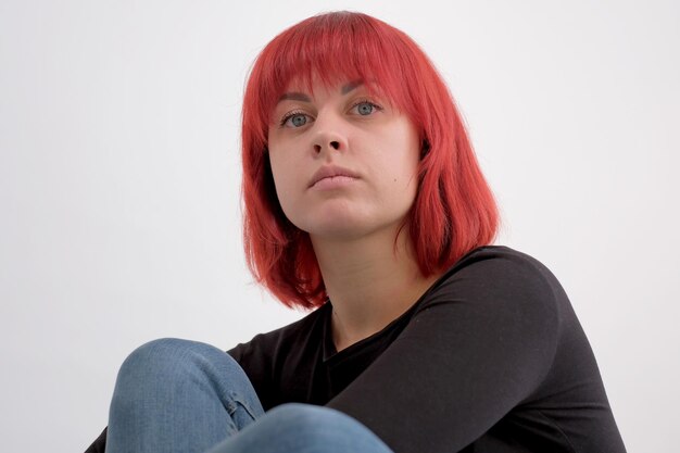 Hermosa mujer joven linda con peinado naranja en jeans sentada posando en el estudio sobre fondo blanco