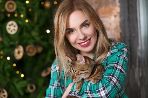 Hermosa mujer joven con lindo gato cerca del árbol de Navidad en casa