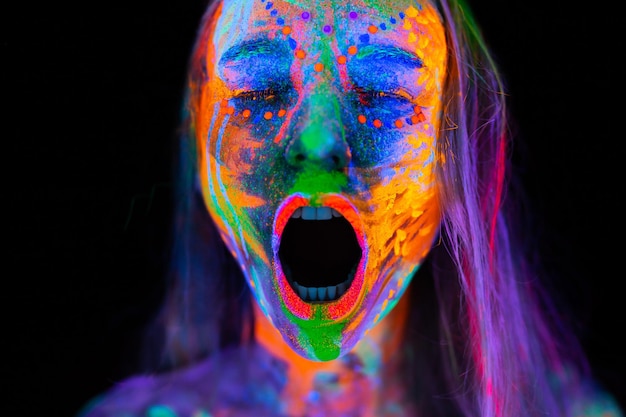 Hermosa mujer joven en luz de neón Retrato de una modelo con maquillaje fluorescente que posa en UV