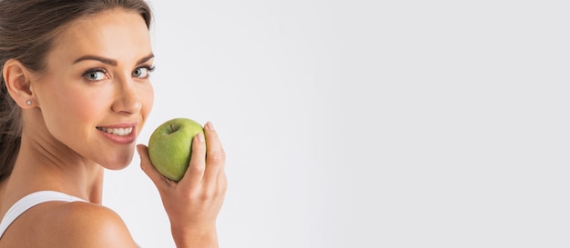 Hermosa mujer joven con manzana verde de cerca en la pared blanca