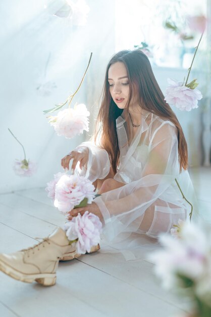 Hermosa mujer joven con maquillaje ligero en colores rosados y cabello rubio sobre un fondo de rosas florecientes Concepto de belleza de niña de primavera