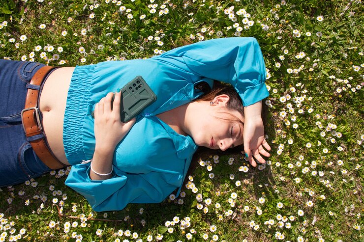 Hermosa mujer joven con marguerites tumbado en la hierba verde con teléfono celular