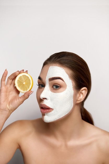 Hermosa mujer joven con máscara blanca de arcilla en la cara piel fresca con rodajas de limón fresco