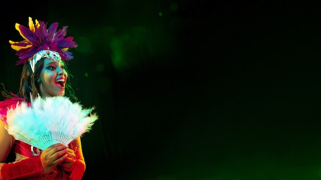 Hermosa mujer joven en máscara de carnaval, elegante traje de mascarada con plumas y bengalas invitando