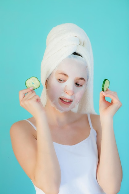 Hermosa mujer joven con máscara facial en la cara sosteniendo rodajas de pepino.