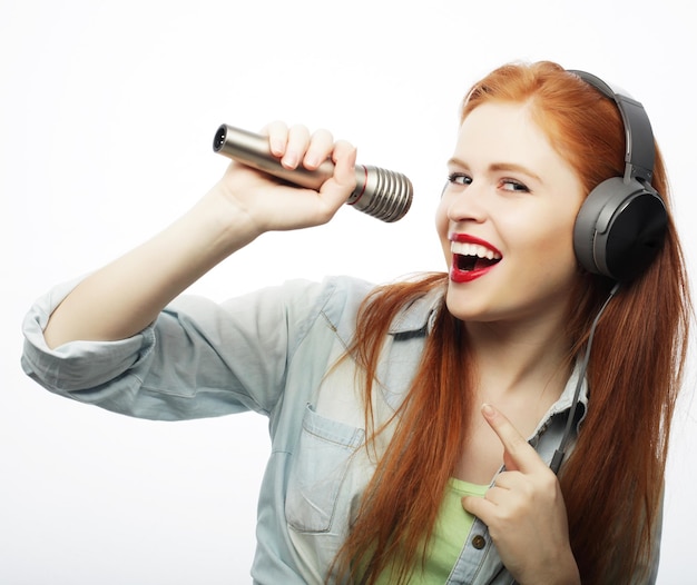 Hermosa mujer joven con micrófono y auriculares sobre fondo gris