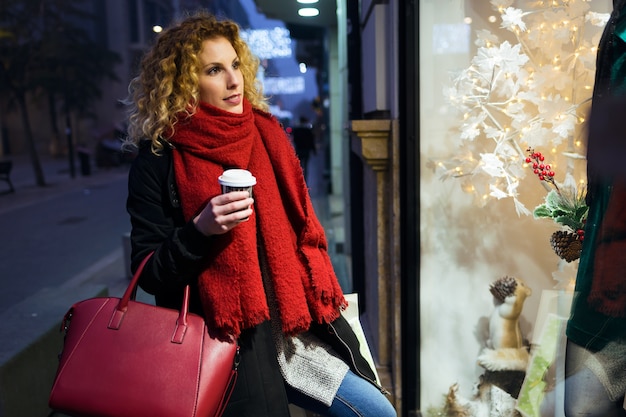 Hermosa mujer joven mirando la ventana de la tienda por la noche.