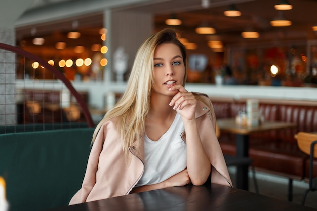 Hermosa mujer joven de moda en una chaqueta rosa de moda está descansando en un café