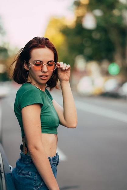 Hermosa mujer joven de moda en gafas posando cerca del coche