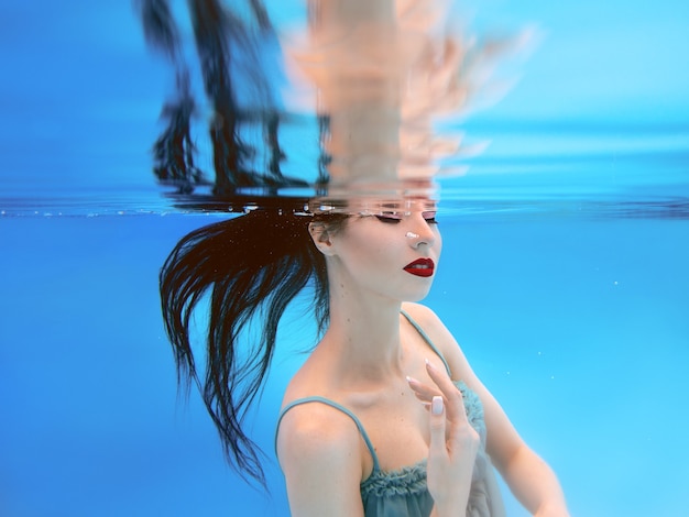 Hermosa mujer joven morena con maquillaje bajo el agua en la piscina