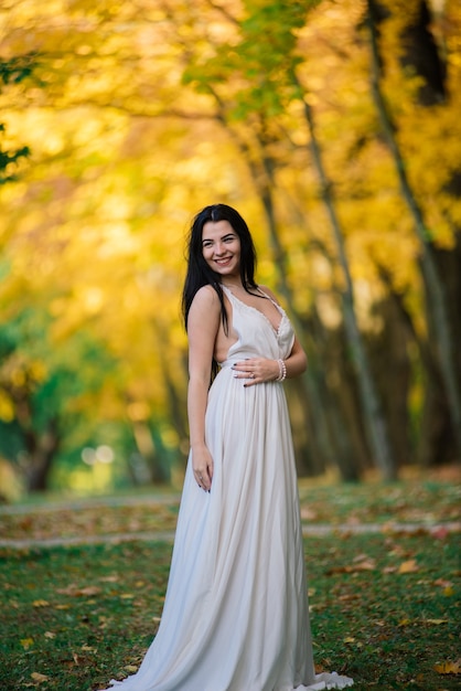 Hermosa mujer joven morena con un vestido blanco en el parque otoño