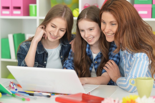 Hermosa mujer joven y niñas sentadas en la mesa y usando una computadora portátil y bebiendo té