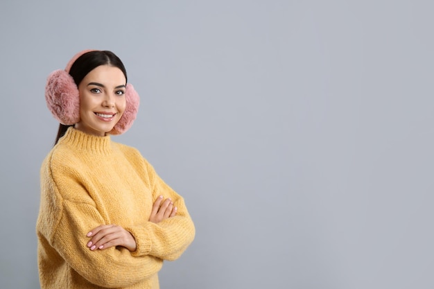 Hermosa mujer joven con orejeras sobre fondo gris claro Espacio para texto