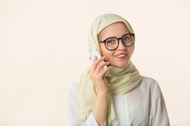 Hermosa mujer joven en un pañuelo musulmán sobre un fondo blanco con un teléfono móvil