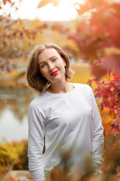 Hermosa mujer joven en el parque otoño. Concepto de temporada y personas. Modelo de moda rubia divirtiéndose en el parque de otoño al aire libre.