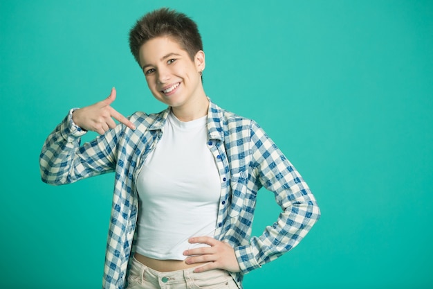 Foto hermosa mujer joven con el pelo corto en una camisa sobre una pared azul apuntando con su dedo