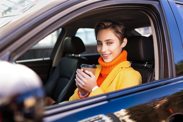 Hermosa mujer joven con el pelo corto conduce un coche en la ciudad