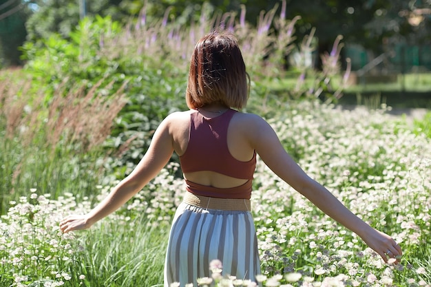 Hermosa mujer joven con pelo largo y rizado vestida con vestido de estilo boho posando en un campo con dientes de León.