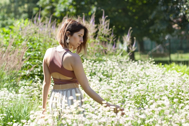 Hermosa mujer joven con pelo largo y rizado vestida con vestido de estilo boho posando en un campo con dientes de León.