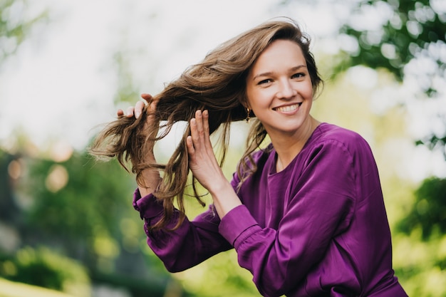 Hermosa mujer joven con el pelo largo vestida con un vestido morado sostiene su cabello