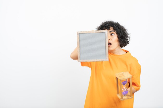 Hermosa mujer joven con pelo rizado con marco con reloj de arena.