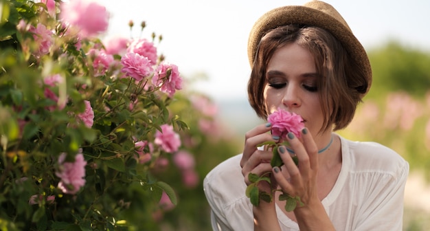 Hermosa mujer joven con pelo rizado posando cerca de rosas en un jardín. El concepto de publicidad de perfumes.