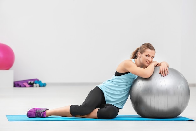 Hermosa mujer joven con pelota de fitness en el gimnasio