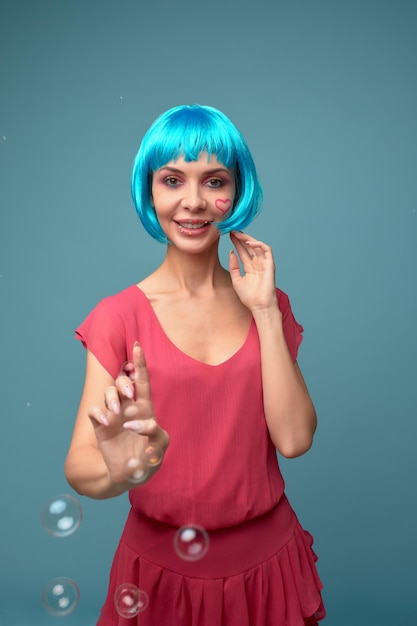 Hermosa mujer joven con peluca azul y maquillaje brillante en pompas de jabón Chica modelo de moda con maquillaje de color creativo Concepto de muñeca de mujer